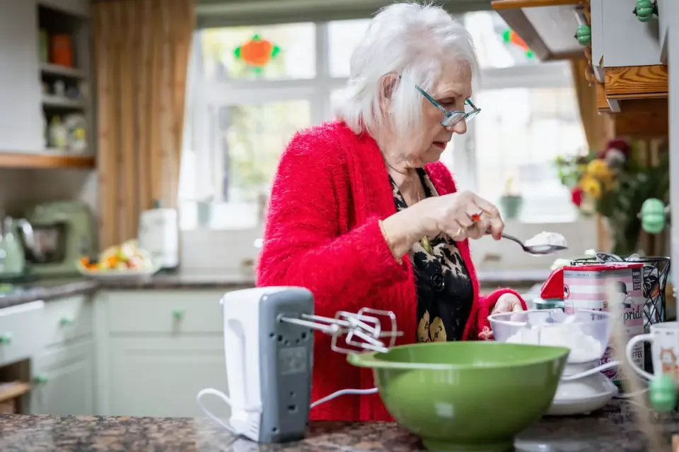 A gray-muzzled senior dog eating from a stainless steel bowl in a kitchen