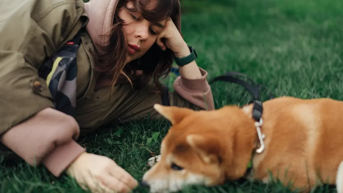 An owner reads a medicine bottle label while a dog rests nearby on a blanket