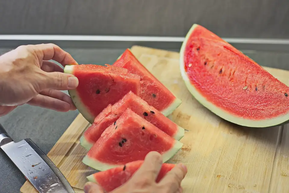 Hands cutting watermelon flesh into small cubes on a cutting board