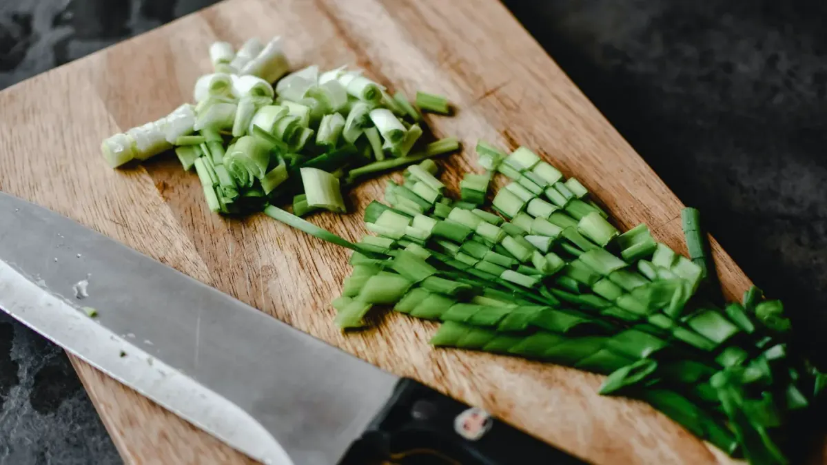 Sliced yellow onion on a wooden cutting board next to a chopping knife